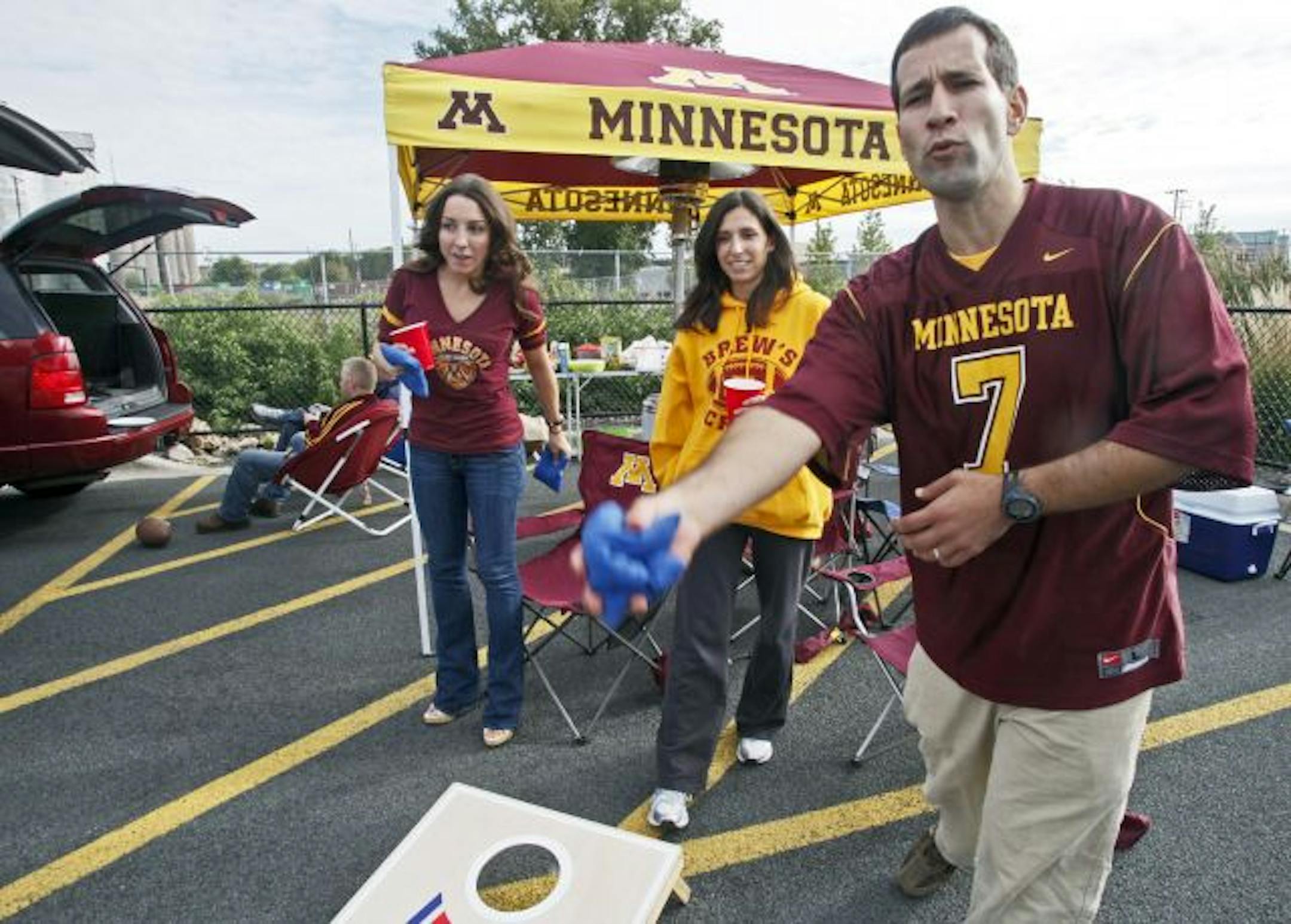 Gophers fans Megan McElroy, Dawn Zouber and Danny Zouber, l-r warm up in a TCF stadium parking lot before the game with drinks and games.