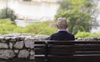 A lonely old man sitting on a bench in a park, looking at river