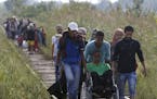Migrants assist a wheelchair user as they all advance along the railway track near the Serbian border with Hungary, near Horgos, Serbia, Tuesday, Aug.