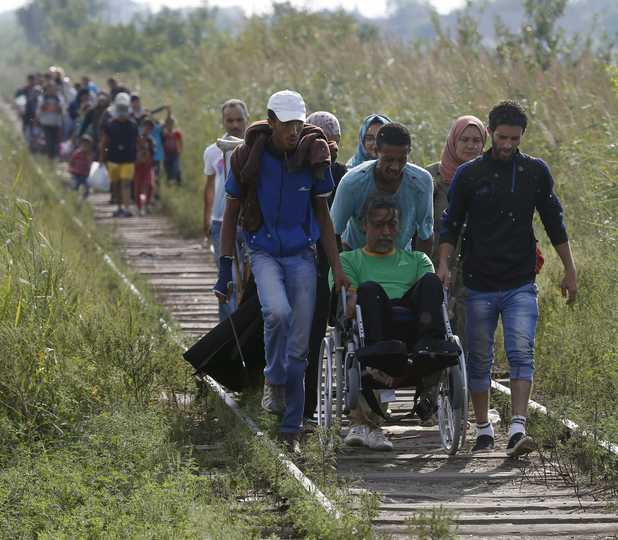 Migrants assist a wheelchair user as they all advance along the railway track near the Serbian border with Hungary, near Horgos, Serbia, Tuesday, Aug. 25, 2015. Thousands of migrants have been crossing into Hungary on their way toward Germany and other rich EU countries as part of a new wave of people fleeing war-thorn countries of the Middle East and Africa. (AP Photo/Darko Vojinovic)