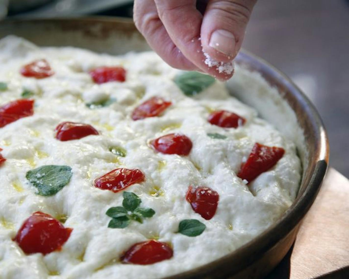 Before baking, the focaccia dough is topped with olive oil, fresh herbs, peppers and coarse salt.