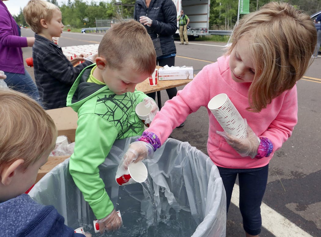 Morgens Leis, 4, (from left), Junes Schmid, 5, and Elizabeth Schmid, 7, fill water cups at the mile 13 checkpoint during the 2017 race.