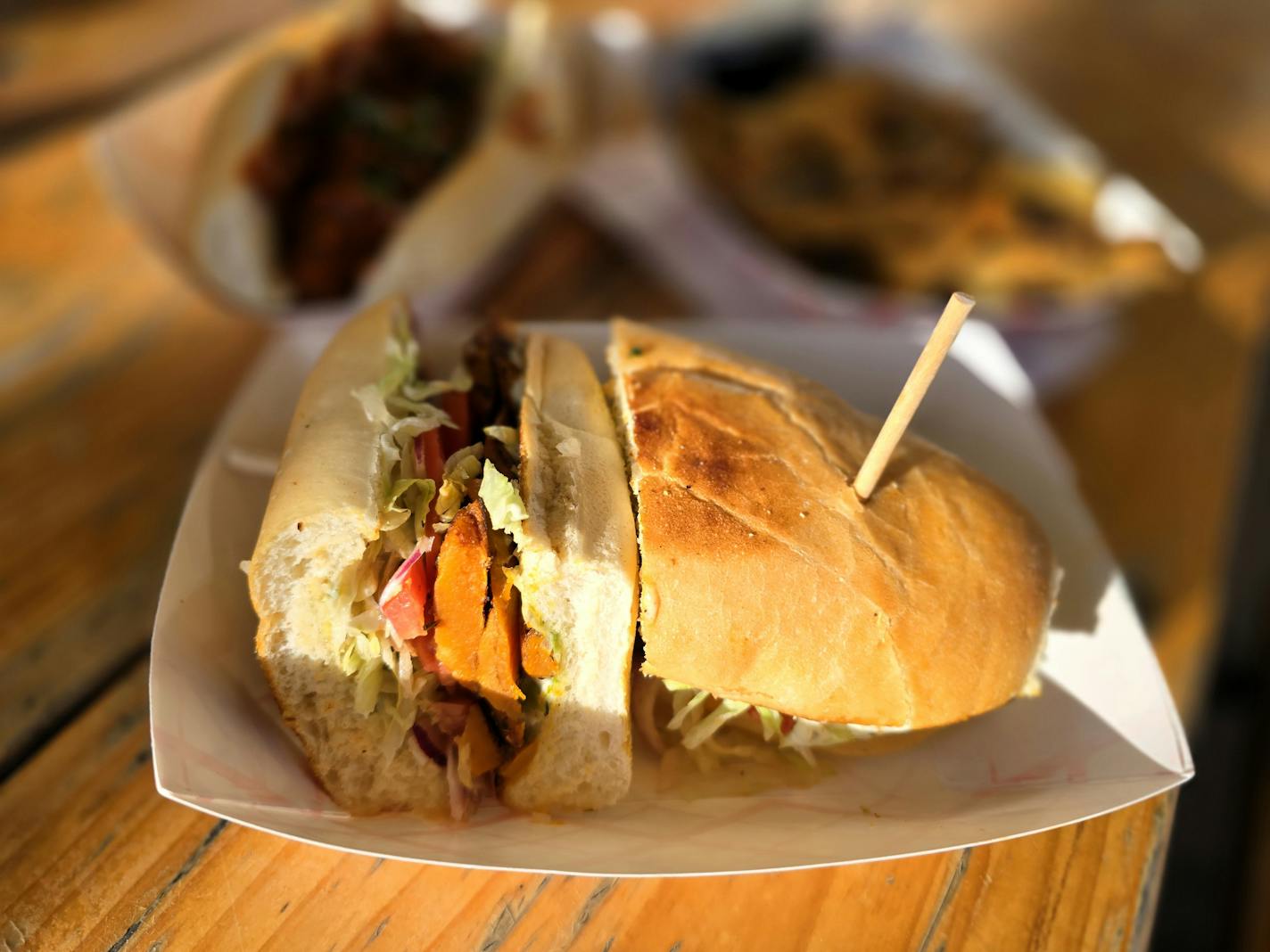 A white sandwich bun is filled with orange slices of sweet potato, served in a basket on a wooden picnic table