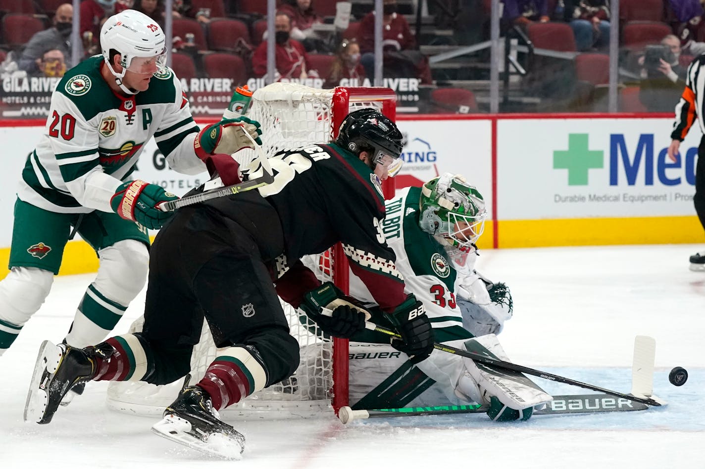 Minnesota Wild goaltender Cam Talbot (33) makes a save on a shot from Arizona Coyotes right wing Christian Fischer as Wild defenseman Ryan Suter (20) shoves Fischer during the first period of an NHL hockey game Wednesday, April 21, 2021, in Glendale, Ariz. (AP Photo/Ross D. Franklin)