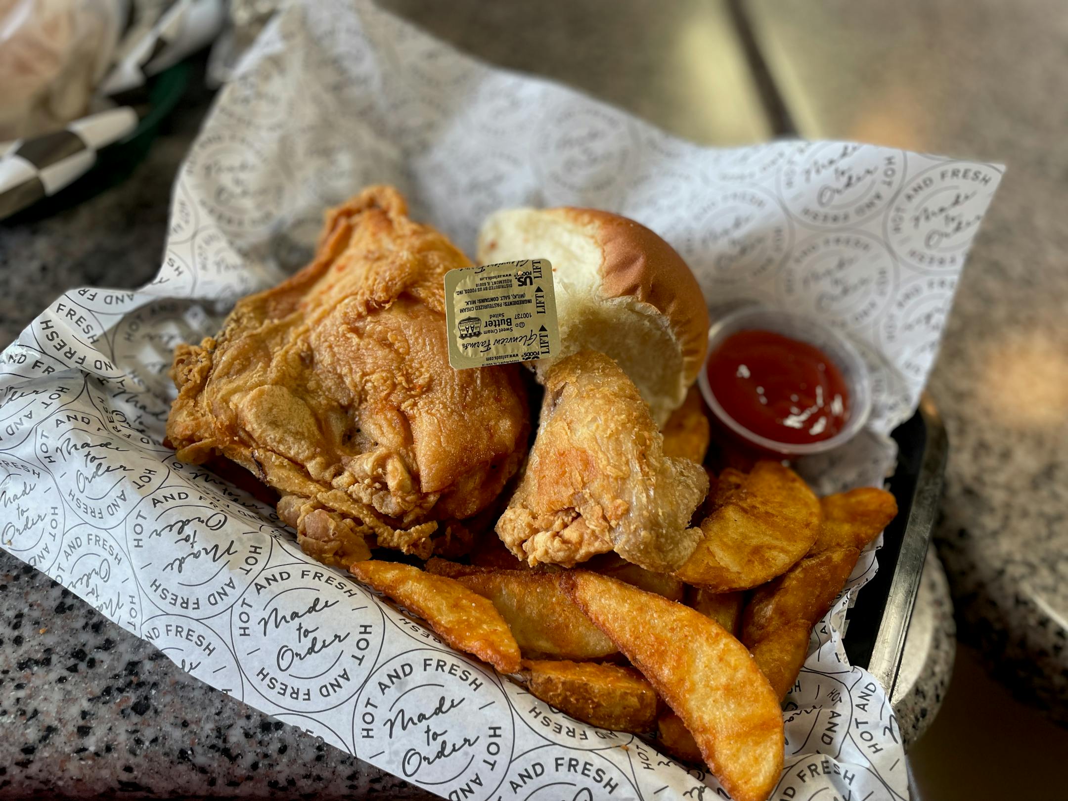 A wing and a breast of fried chicken and potato wedges with a roll.