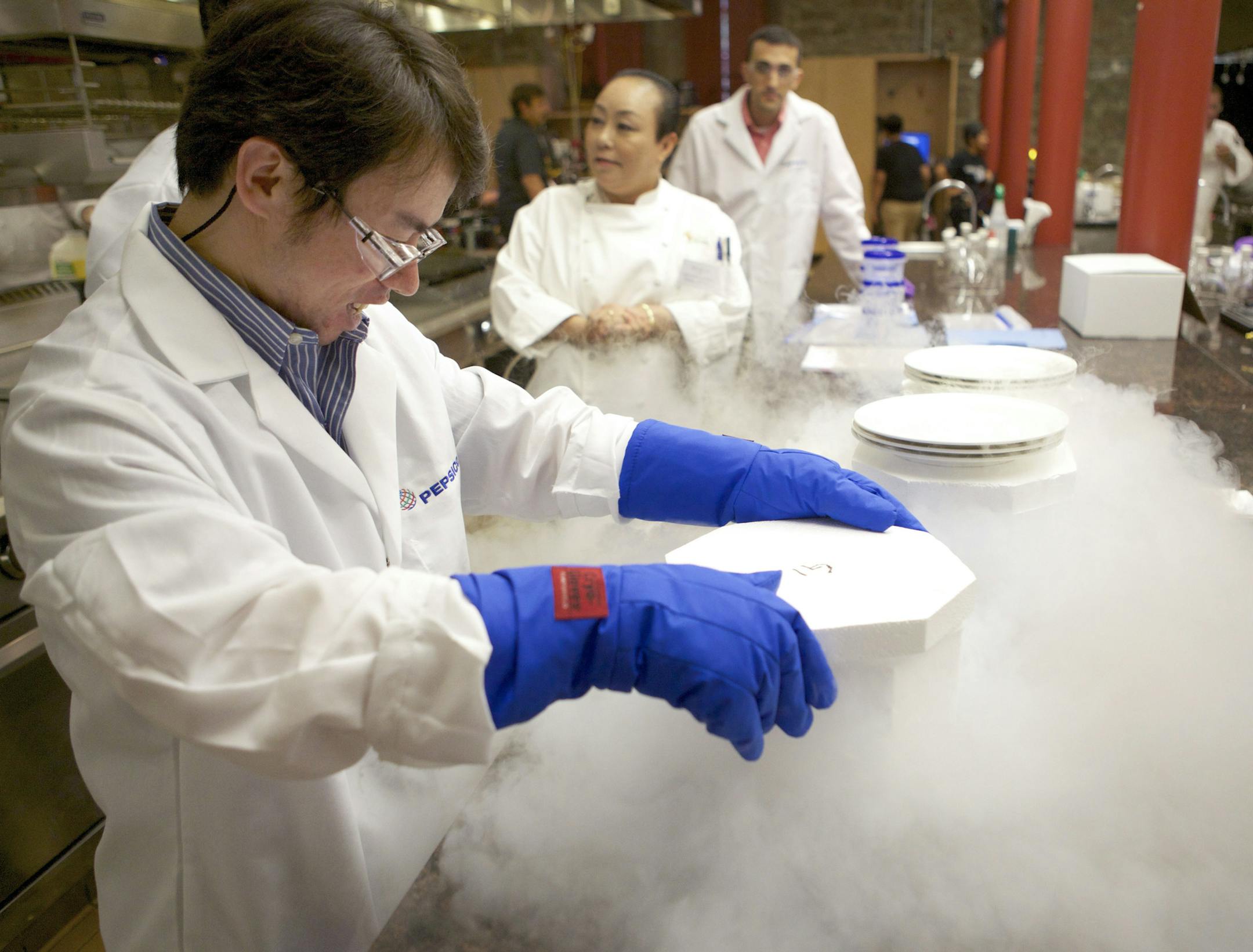 Yanpeng Hou, left, of PepsiCo, places a bowl of tofu soup into a container of liquid nitrogen to freeze it for later testing at The Culinary Institute of America at Greystone in St. Helena, Calif., June 26, 2013. At companies like PepsiCo and Kellogg, white-coated lab technicians join with white-jacketed chefs to give consumers the taste they want with less salt, fat and sugar. (Thor Swift/The New York Times)