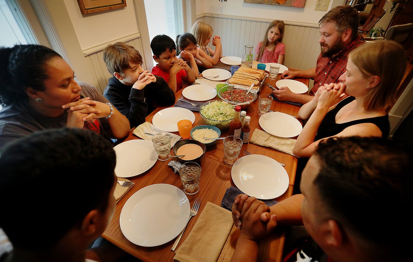 The families of Honduran refugee Nuria Arias, left, and Ry Siggelkow, a Mennonite pastor, third from right, who was hosting Arias and her three children, sat down for dinner together and listened to Siggelkow read a prayer in Spanish on his smart phone before the meal Saturday, Aug. 4, 2018, in Minneapolis, MN. Arias had prepared the meal of chicken flautas, a favorite of her family back in Honduras.] DAVID JOLES &#xef; david.joles@startribune.com A refugee family from Honduras recounts their li