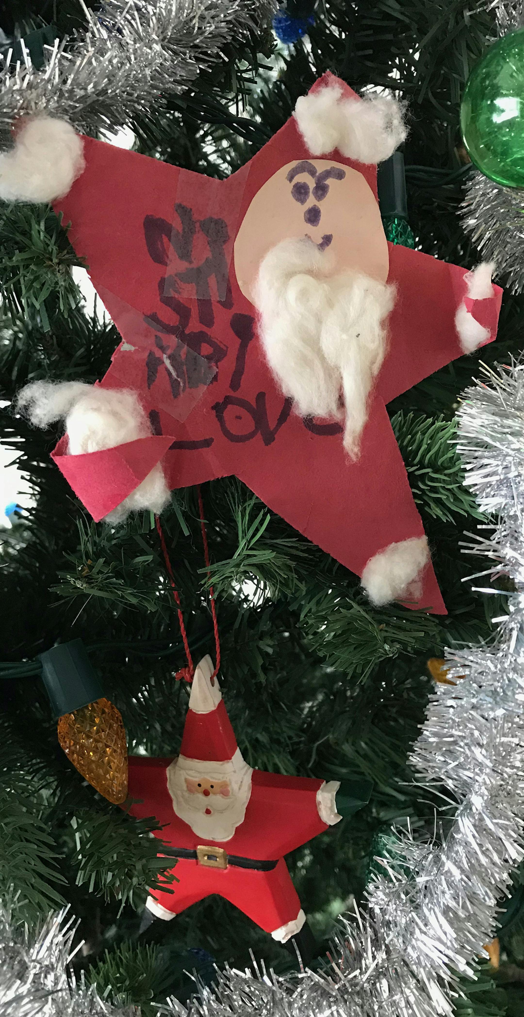 "My daughter made this 5 star construction paper Santa in 1981. She wrote Love Kristin (from the bottom up) in her best Kindergarten printing.
It immediately was placed on our Christmas tree and then carefully tucked away for the next Christmas. When she was in high school, she bought me the 5 star Santa ornament (seen in the picture) in hopes I'd toss her handmade one and replace it with the new one. Little did she know then that the construction paper Santa could never be replaced. Both hang o