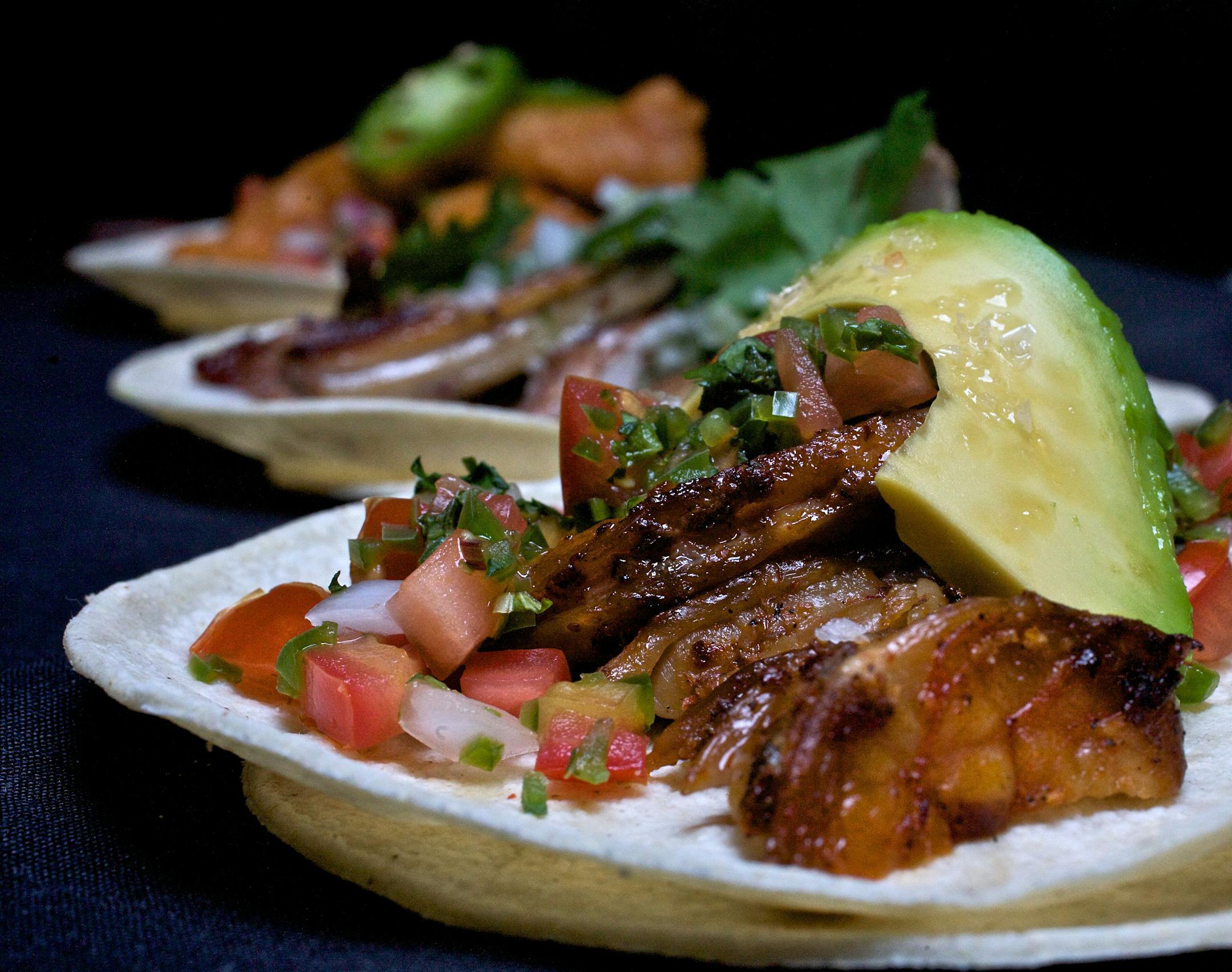 Three tacos rest on double tortillas at Barrio:: Port Carnitas taco with Serrano chile salsa, the Grilled Skirt Steak with roasted poblano rajas and the fried Mahi Mahi taco with citrus-cucumber pico de gallo.