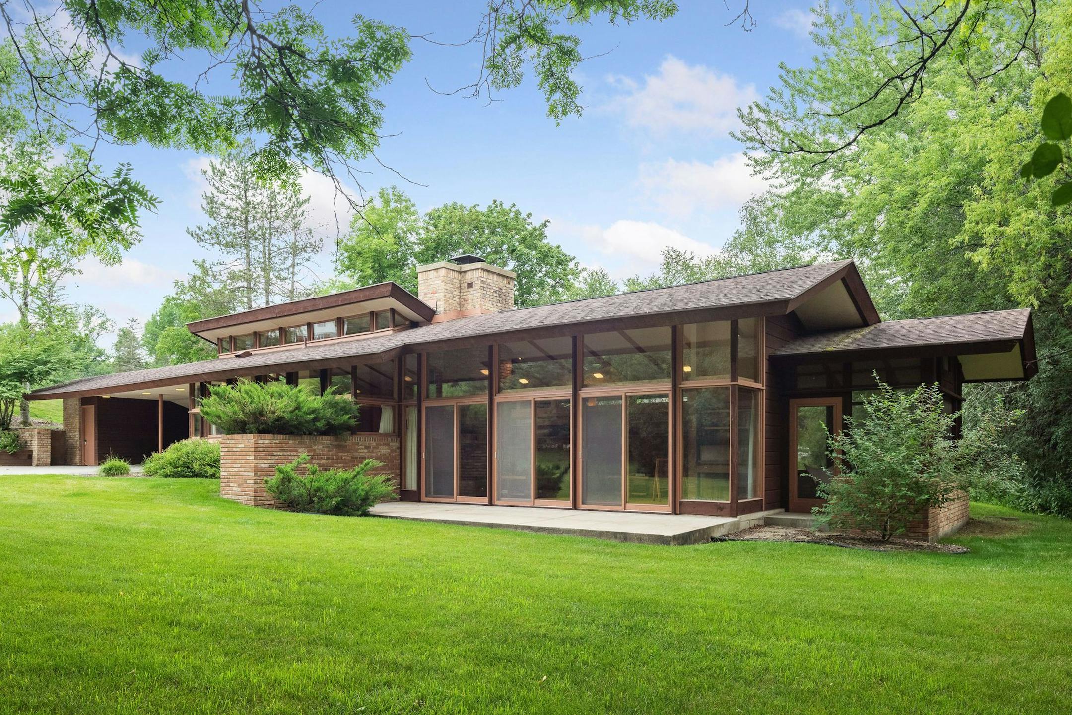 A low-slung one-story house designed by Frank Lloyd Wright associated John Howe is nestled into a hillside in Rochester.