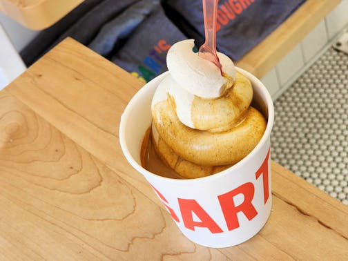 A paper cup with orange writing sits on a counter, containing a tall swirl of off-white soft-serve coated in caramel-colored espresso