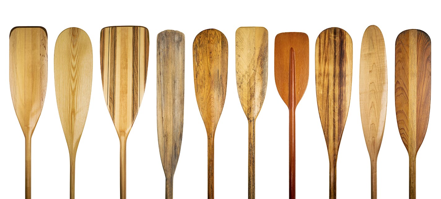 a row of 10 wooden canoe paddles, a variety of styles and shapes - paddling concept