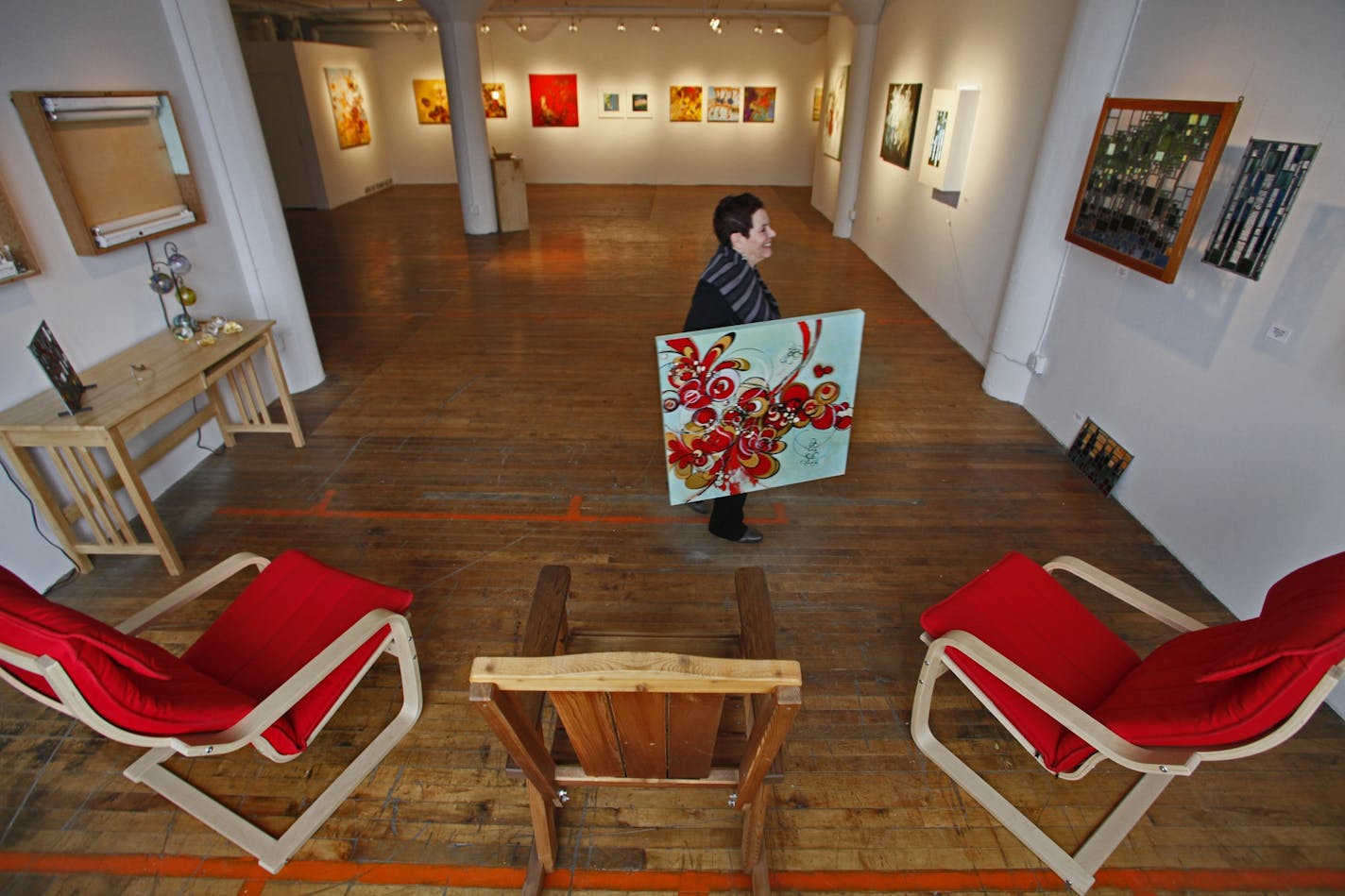 Anita Sue Kolman in the Kolman Gallery carrying a painting by Patrick Kemal Pryor.