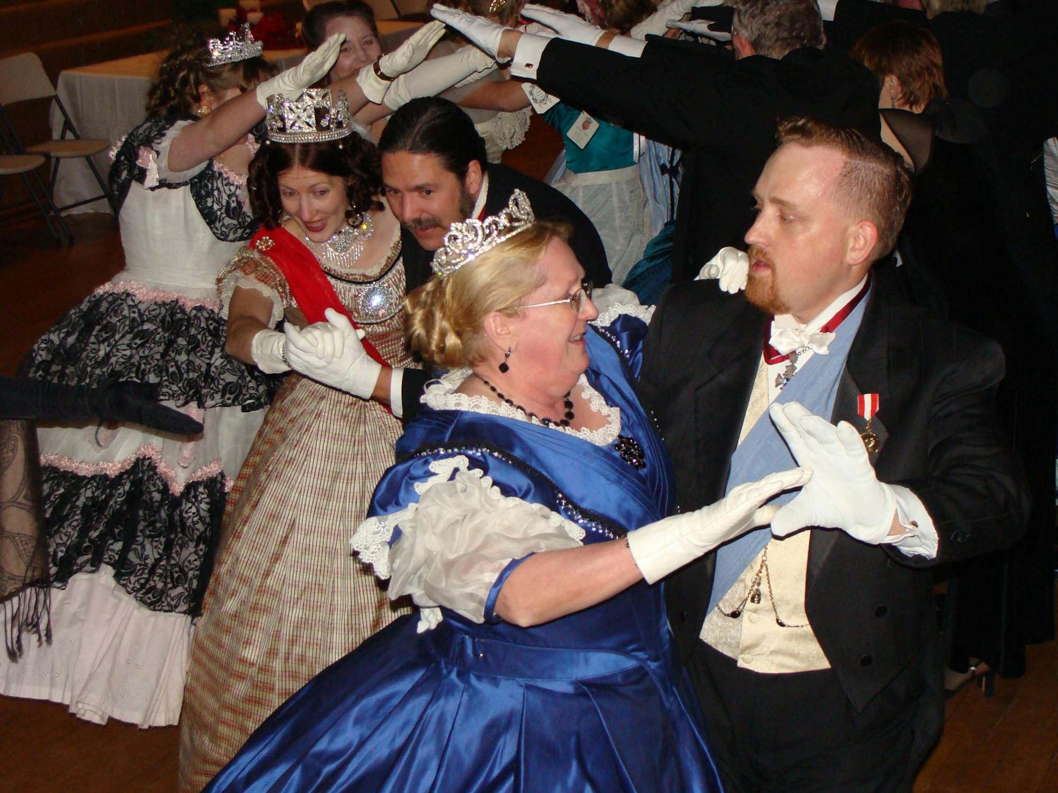"Twelfth Night Gala" given by the Victorian Society of America's local chapter. Leading the way, Kit Cusick (far right) danced with his partner Kathryn Wakal, who wore a dress that Cusick designed. They were followed by the royal couple Queen Victoria, Regina (played by Christie Kopitzke) and Prince Albert (Joseph Manussier). The Grand March is the traditional first dance.
