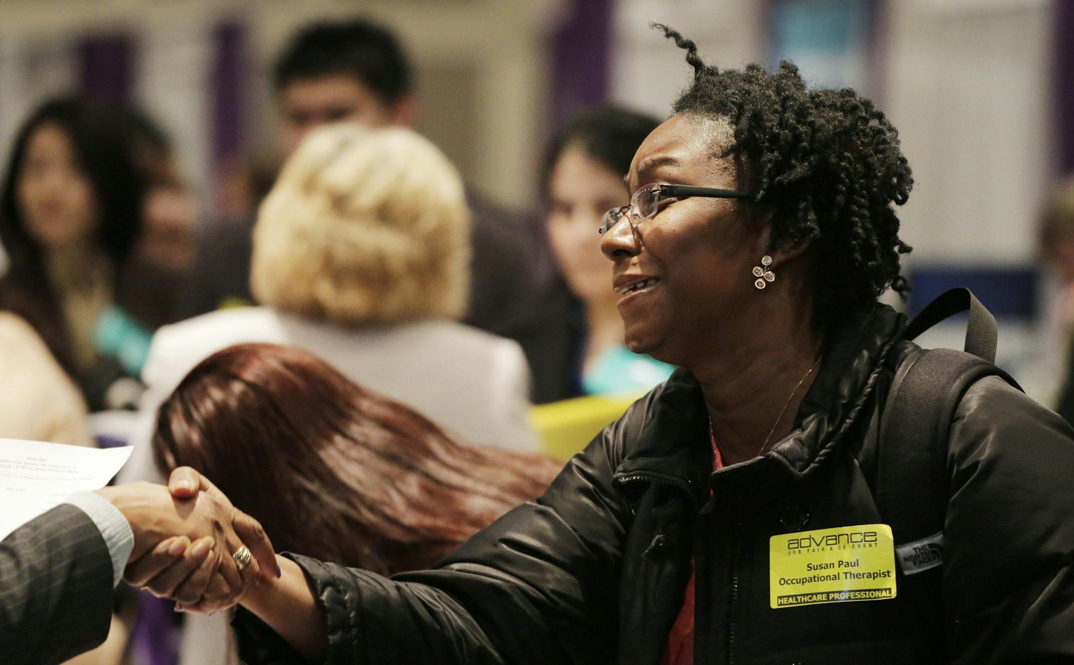 Susan Paul, who has recently completed a Masters program in occupational therapy, shakes hands with a recruiter at a healthcare job fair, Thursday, March 14, 2013 in New York. Fewer Americans sought unemployment aid last week, reducing the average number of weekly applications last month to a five-year low. The drop shows that fewer layoffs are strengthening the job market. The Labor Department said Thursday that applications fell 10,000 to a seasonally adjusted 332,000. That cut the four-week a