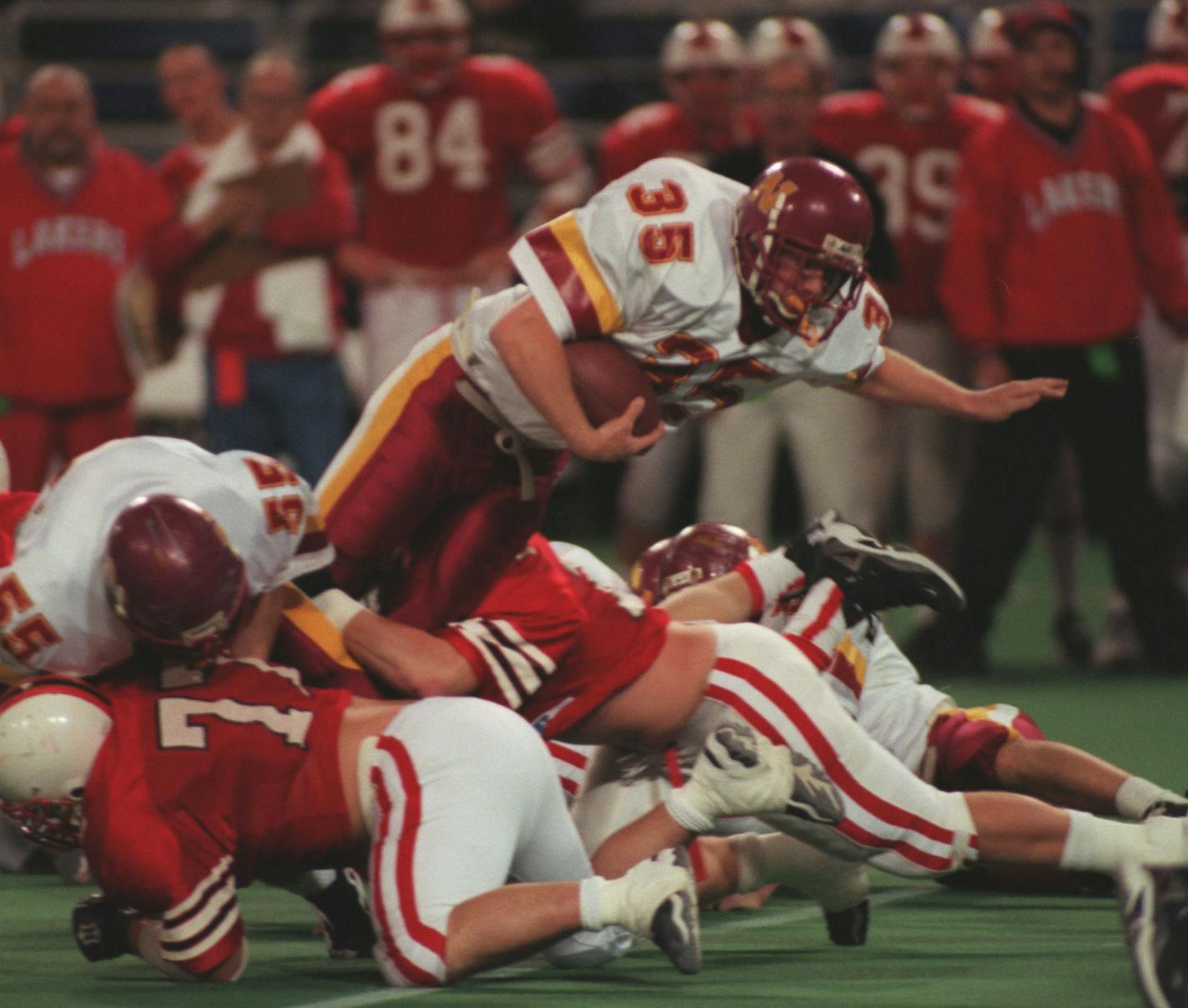 Northfield vs Detroit Lakes — Northfield running back Matt Geiger leaps over a pile of Detroit Lakes players during the first quarter of the section 4A championship game at the Metrodome. Geiger went on to score three touchdowns and recovered a fumble as the Raiders beat the Lakers 28-0.