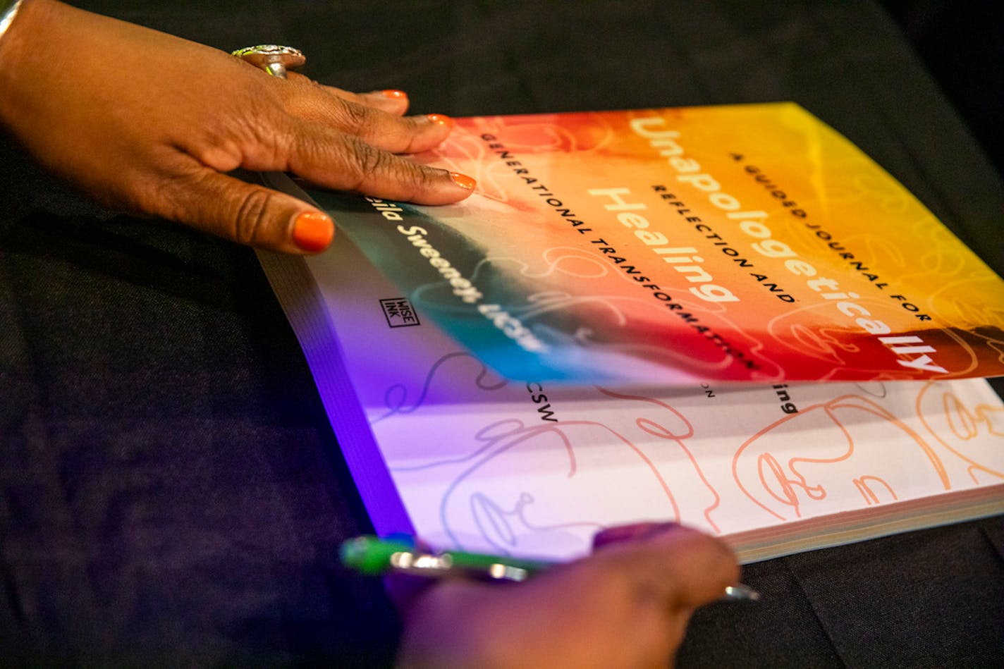 Picture of book held by two hands, one with a pen.