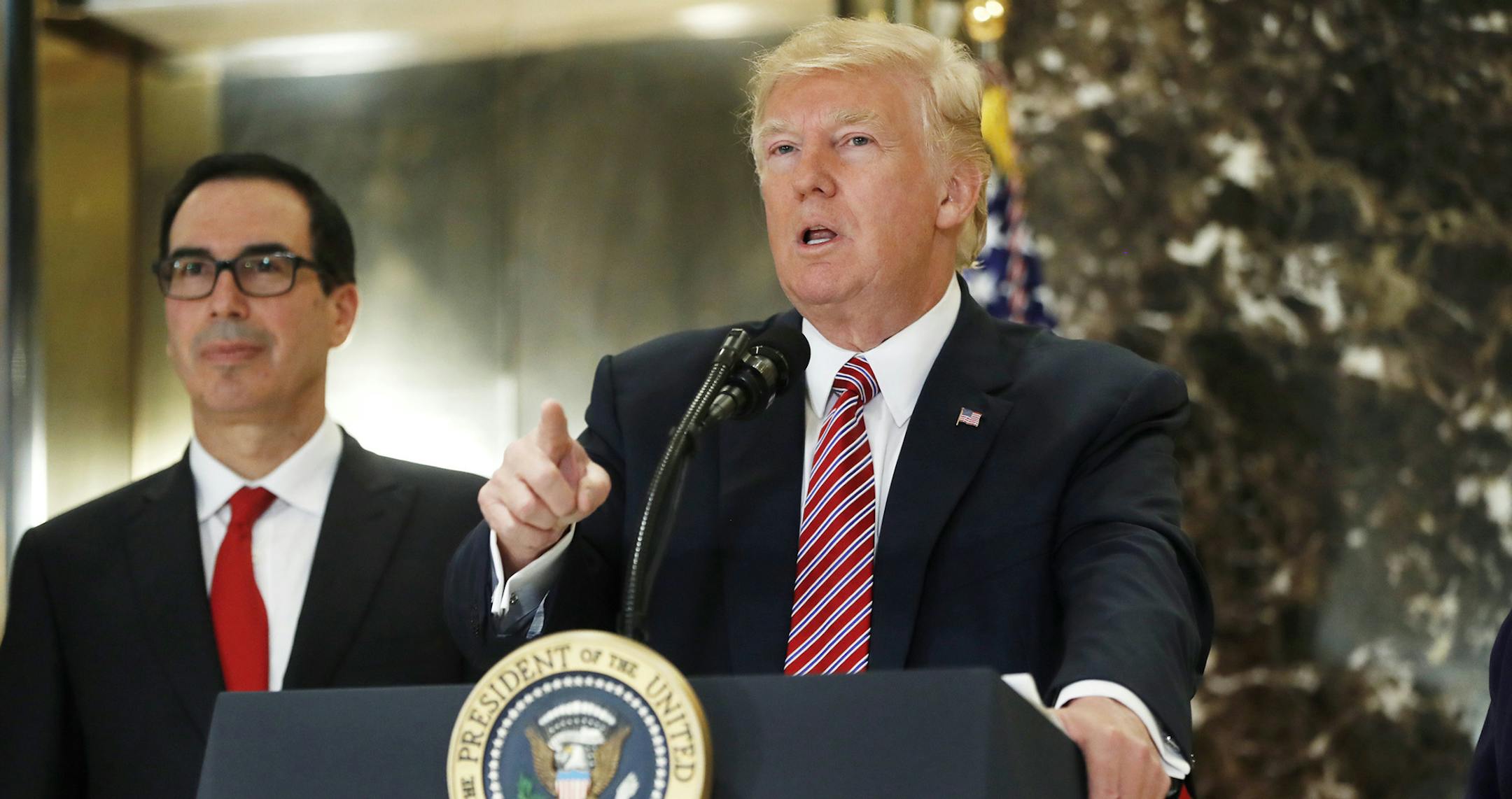 President Donald Trump, accompanied by Treasury Secretary Steven Mnuchin, speaks to the media in the lobby of Trump Tower in New York, Tuesday, Aug. 15, 2017.