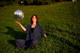 Emma Dalenberg sitting on grassy lawn bouncing metallic ball.