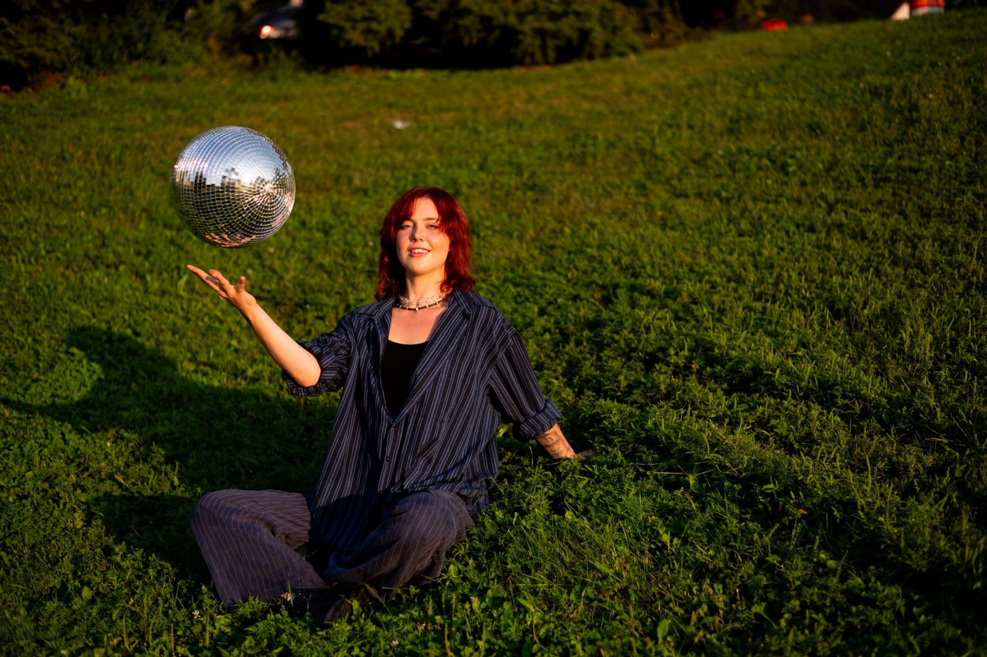 Emma Dalenberg sitting on grassy lawn bouncing metallic ball.