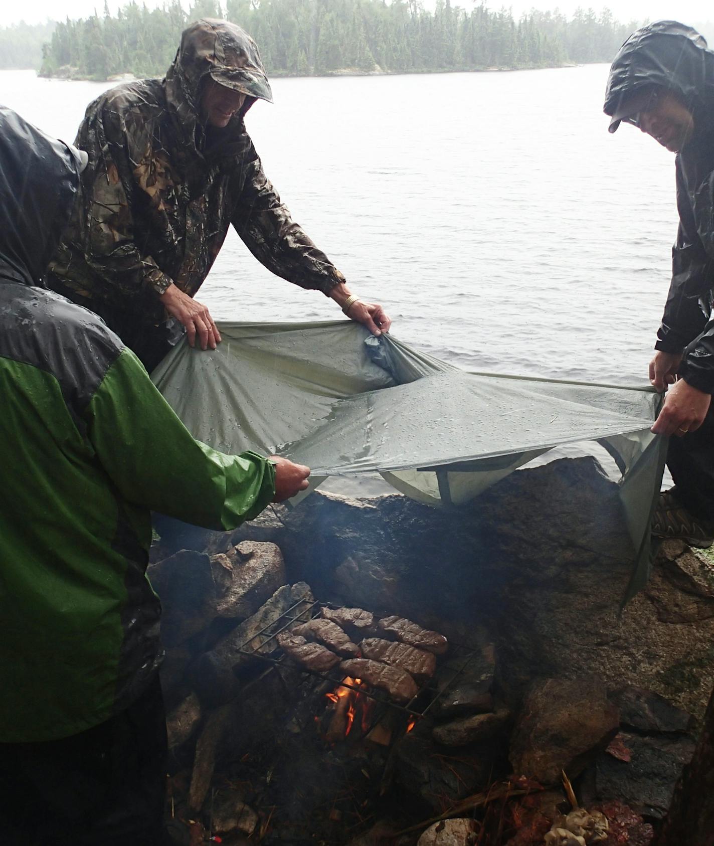 Campers hold a plastic poncho over a campfire as they try to finish cooking steaks during a rainstorm. Greg Swenson, right, later fell from his perch on the rock, but wasn't seriously hurt. Star Tribune photo by Doug Smith