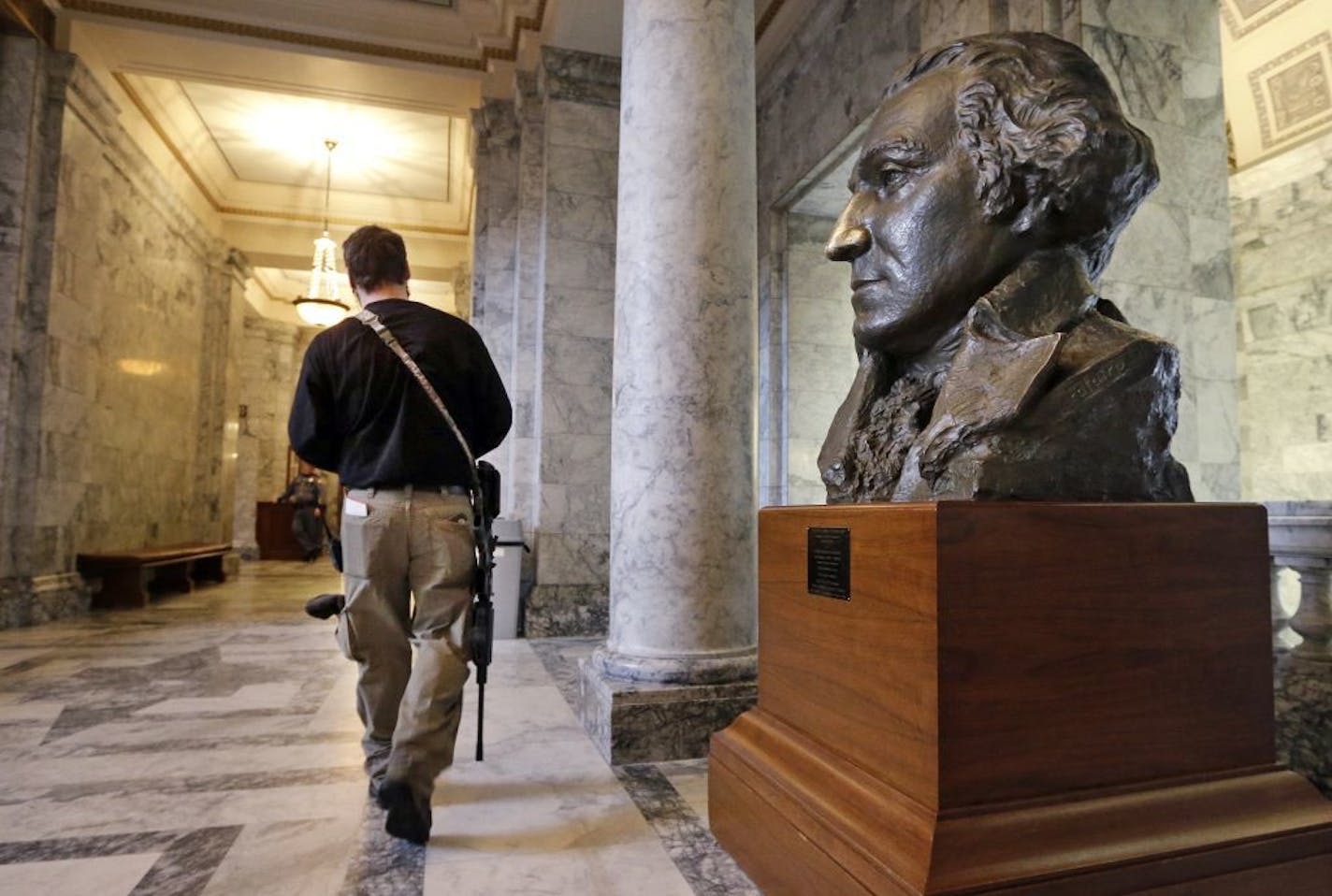 Kevin King, of Graham, Wash., carries an AR-15 rifle as he walks past a bust of George Washington in the Capitol rotunda following a gun rights rally on the steps outside Jan. 15, 2016, in Olympia, Wash. Lawmakers and others spoke at the rally, which drew about 100 people, emphasizing legislative priorities and speaking against gun-related policies of President Barack Obama, like his recent executive actions to expand background checks to cover more firearms sold at gun shows, and elsewhere.