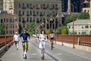 Forrest Morey, left, and Isabella Shelton, right, take in the warm weather on scooters over the Stone Arch Bridge in Minneapolis, Minn., on Monday, Ju