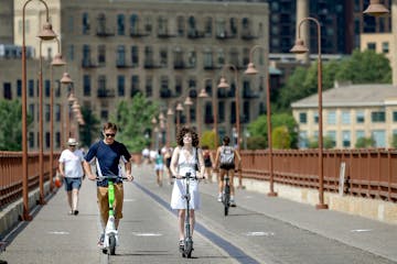 Forrest Morey, left, and Isabella Shelton, right, take in the warm weather on scooters over the Stone Arch Bridge in Minneapolis, Minn., on Monday, Ju