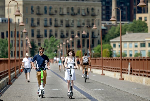 Forrest Morey, left, and Isabella Shelton, right, take in the warm weather on scooters over the Stone Arch Bridge in Minneapolis, Minn., on Monday, Ju