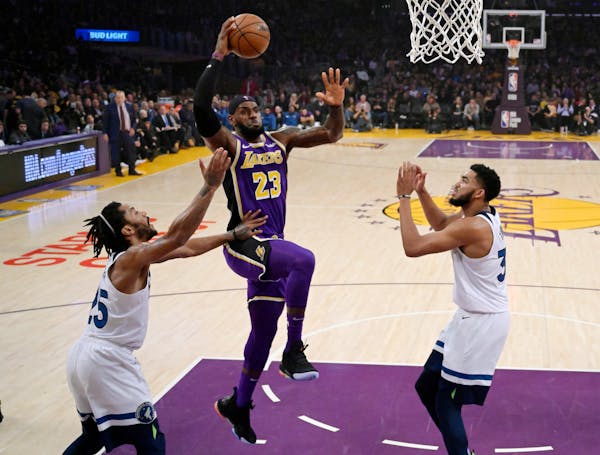 Lakers forward LeBron James, center, shoots as Timberwolves guard Derrick Rose, left, and center Karl-Anthony Towns defend Wednesday at Staples Center