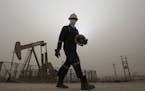 FILE - In this Thursday, Jan. 8, 2015 file photo, an oil worker walks by an oil pump during a sandstorm that blew in, in the desert oil fields of Sakh