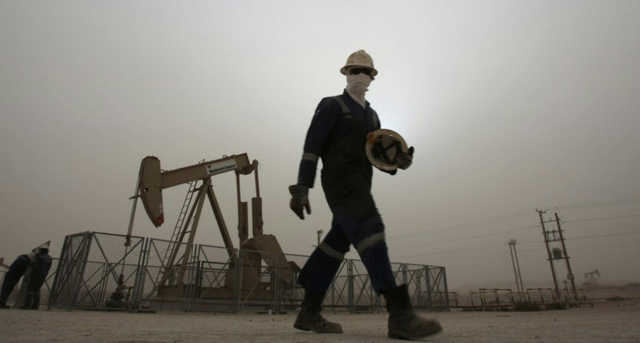 FILE - In this Thursday, Jan. 8, 2015 file photo, an oil worker walks by an oil pump during a sandstorm that blew in, in the desert oil fields of Sakhir, Bahrain. Across a Mideast fueled by oil production, low global prices have some countries running on empty and scrambling to cover shortfalls, even as more regional crude is on tap to enter the market.(AP Photo/Hasan Jamali, File)