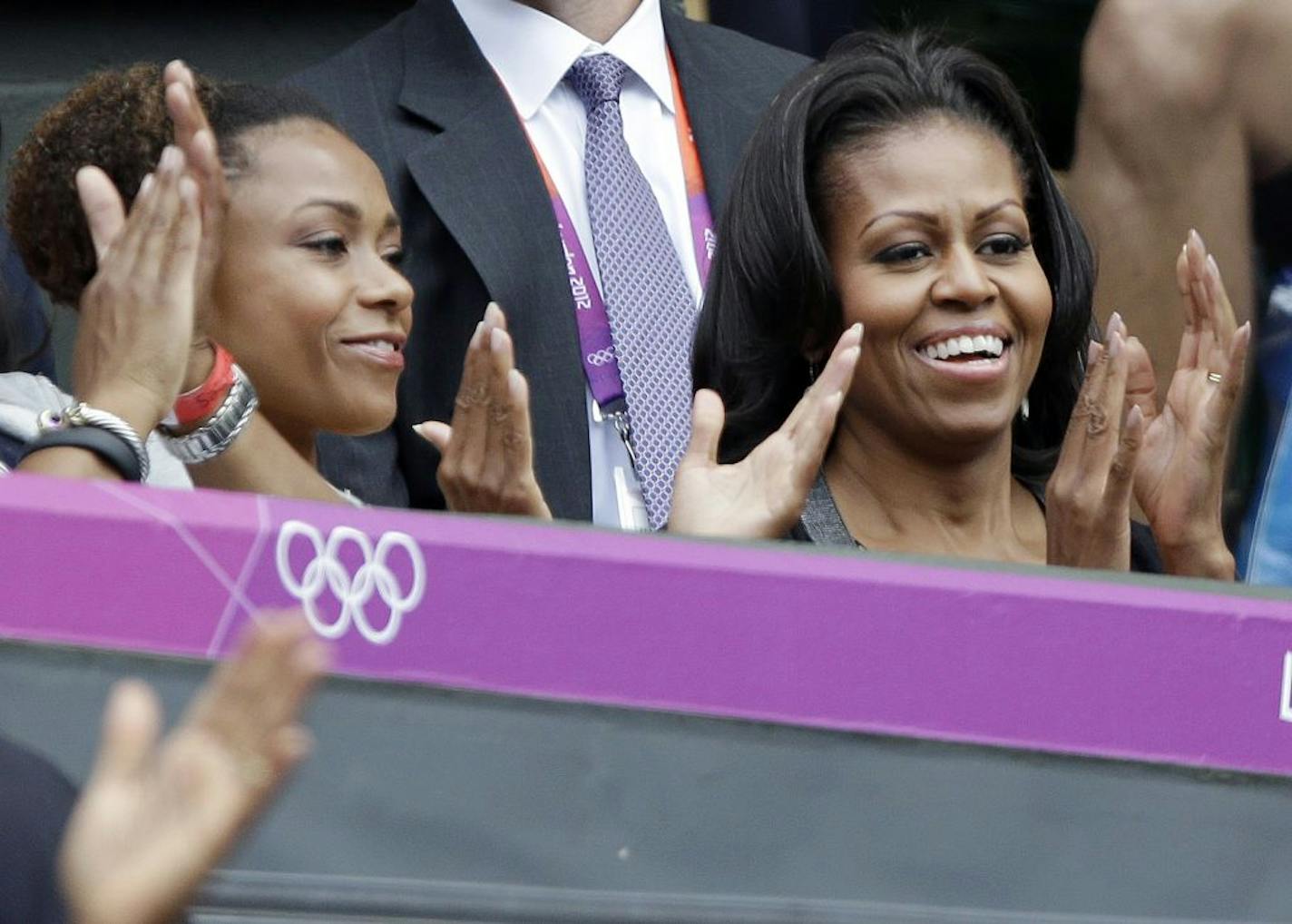 First lady Michelle Obama, right, applauds with former USA gymnast Dominique Dawes as they watch Serena Williams of the United States compete against Jelena Jankovic of Serbia at the All England Lawn Tennis Club in Wimbledon, London at the 2012 Summer Olympics, Saturday, July 28, 2012.