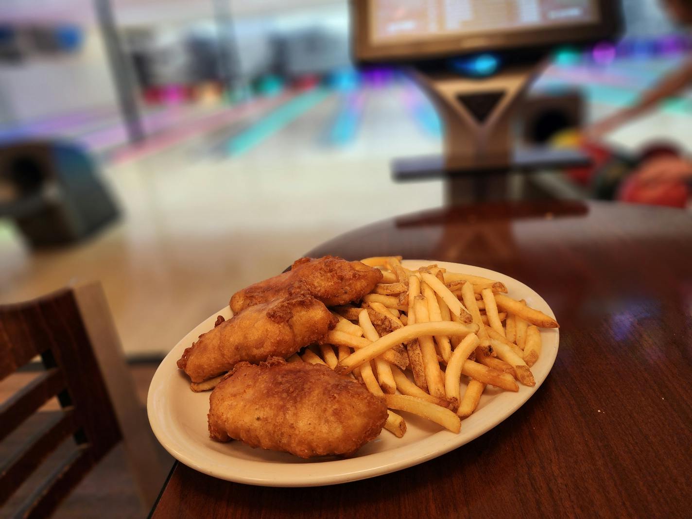 A plate of fried fish and fries in front of colorful bowling lanes