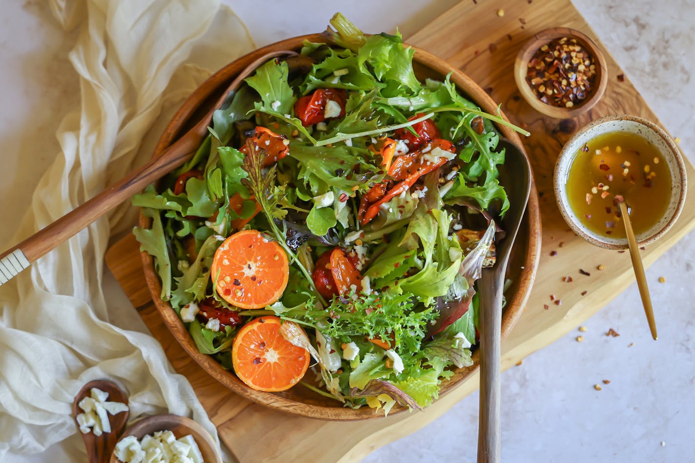 A big platter of salad greens topped with roasted vegetables, orange slice and hot honey vinaigrette, with more hot honey in a bowl off to the side.