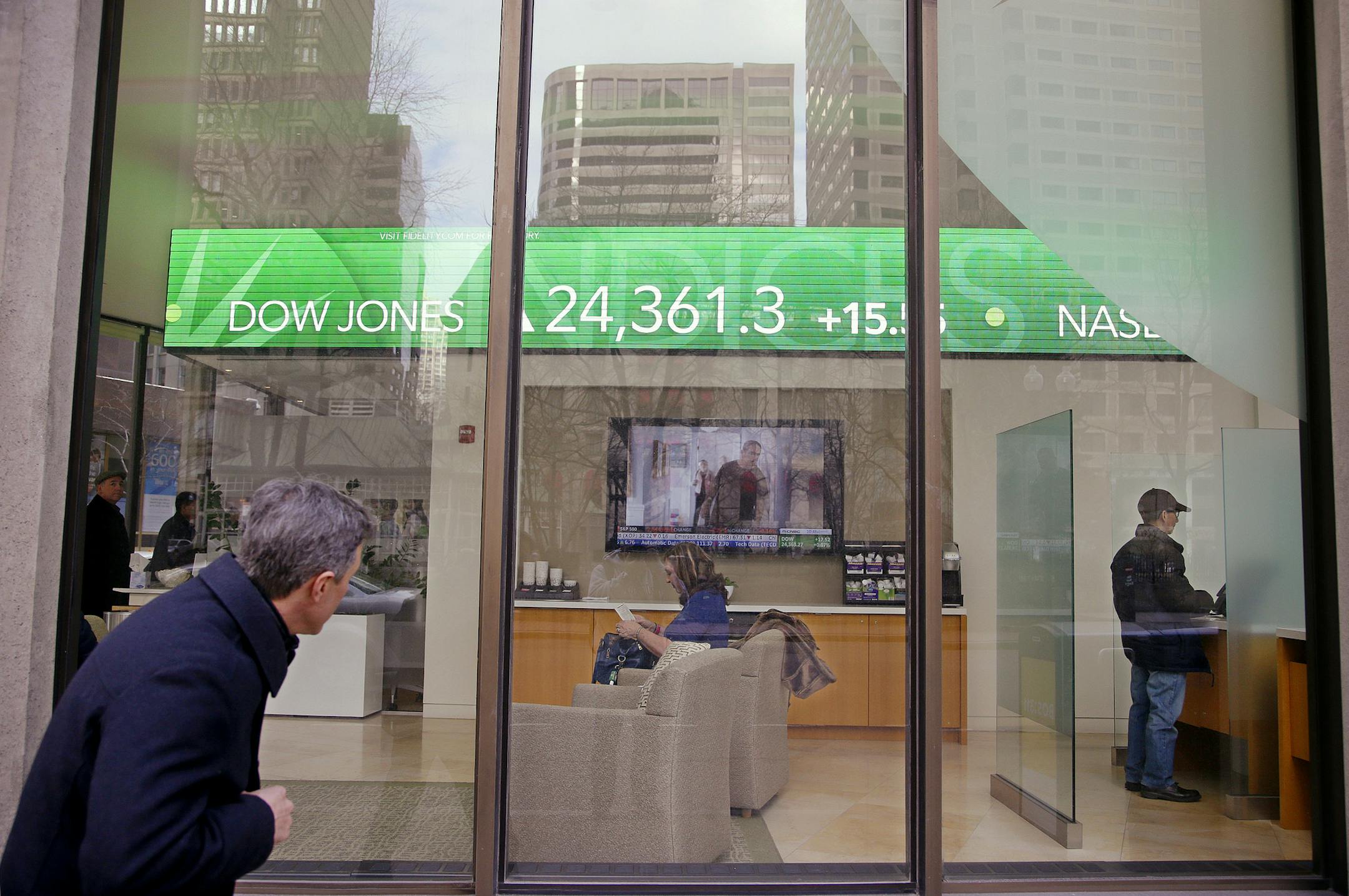 FILE- In this Feb. 6, 2018, file photo, a passer-by peers in the window while investors congregate inside at the Fidelity Investments office on Congress Street as the ticker displays stock market numbers in Boston. A plunge in stock prices always stings, but this recent one dug deeper because more of the country has become exposed to the ups and downs of the market, particularly older Americans. (AP Photo/Stephan Savoia, File)