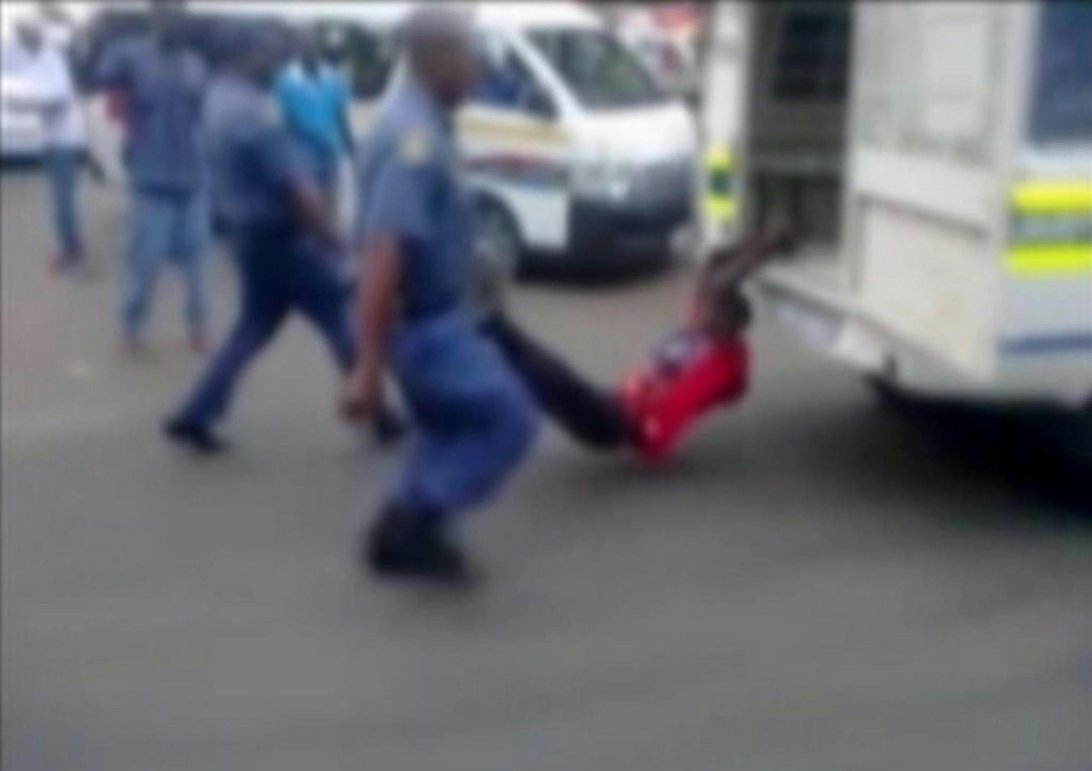 In this still frame from TV and courtesy of South African Daily Sun newspaper, showing a South African man with his hands tethered to the back of a police vehicle being dragged behind as police hold his legs up and the vehicle apparently drives off, east of Johannesburg Tuesday Feb. 26, 2013. The man died of his injuries. In video filmed on a mobile phone, uniformed police are seen trying to subdue the man, then tethering him to the back of a police vehicle which drives off, watched by a large c
