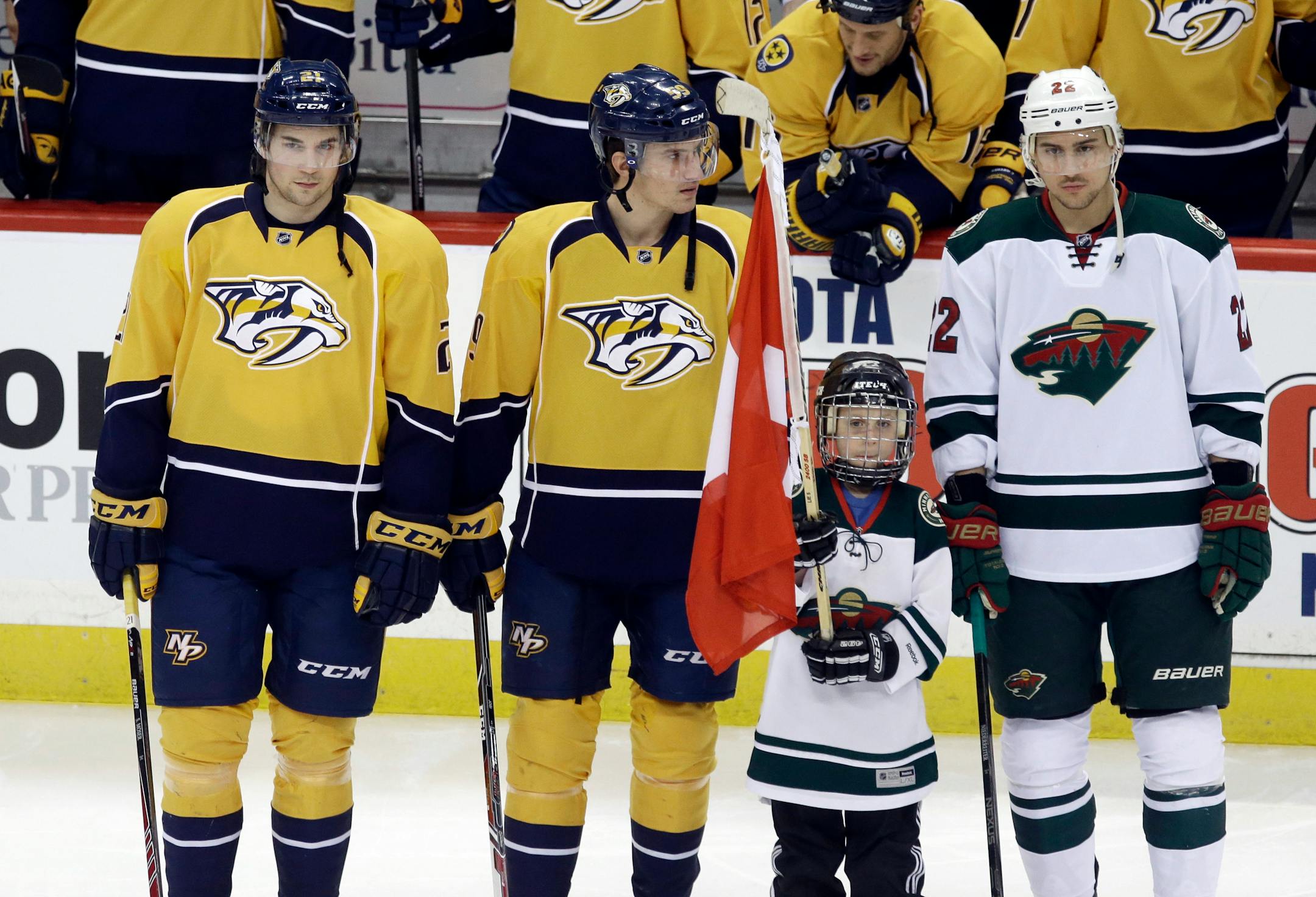 A young flag bearer holds a Swiss flag as Nashville Predators' Simon Moser, left, and Nashville Predators' Roman Josi were honored along with Minnesota Wild's Nino Niederreiter, right, in Olympic sendoff ceremonies prior to an NHL hockey game, Thursday, Feb. 6, 2014, in St. Paul, Minn. The three will play for Switzerland. (AP Photo/Jim Mone)