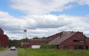 A truck drives past rusted and vacant buildings on July 6, 2023, at a former iron ore processing plant near Hoyt Lakes, Minn.