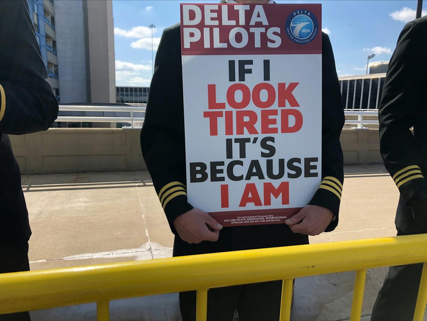 Delta pilots picket at MSP Airport because of record overtime. Picket sign says: If I look tired, it's because I am.