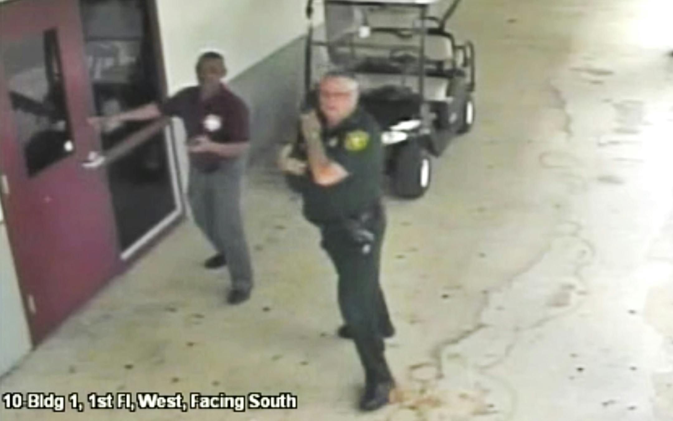 This Feb. 14, 2018 frame from security video provided by the Broward County Sheriff's Office shows deputy Scot Peterson, right, outside Marjory Stoneman Douglas High School in Parkland, Fla. The video released Thursday, March 15, shows Peterson going toward the high school building while a gunman massacred 17 students and staff members, but stayed outside with his handgun drawn. (Courtesy of the Broward County Sheriff's Office via AP)