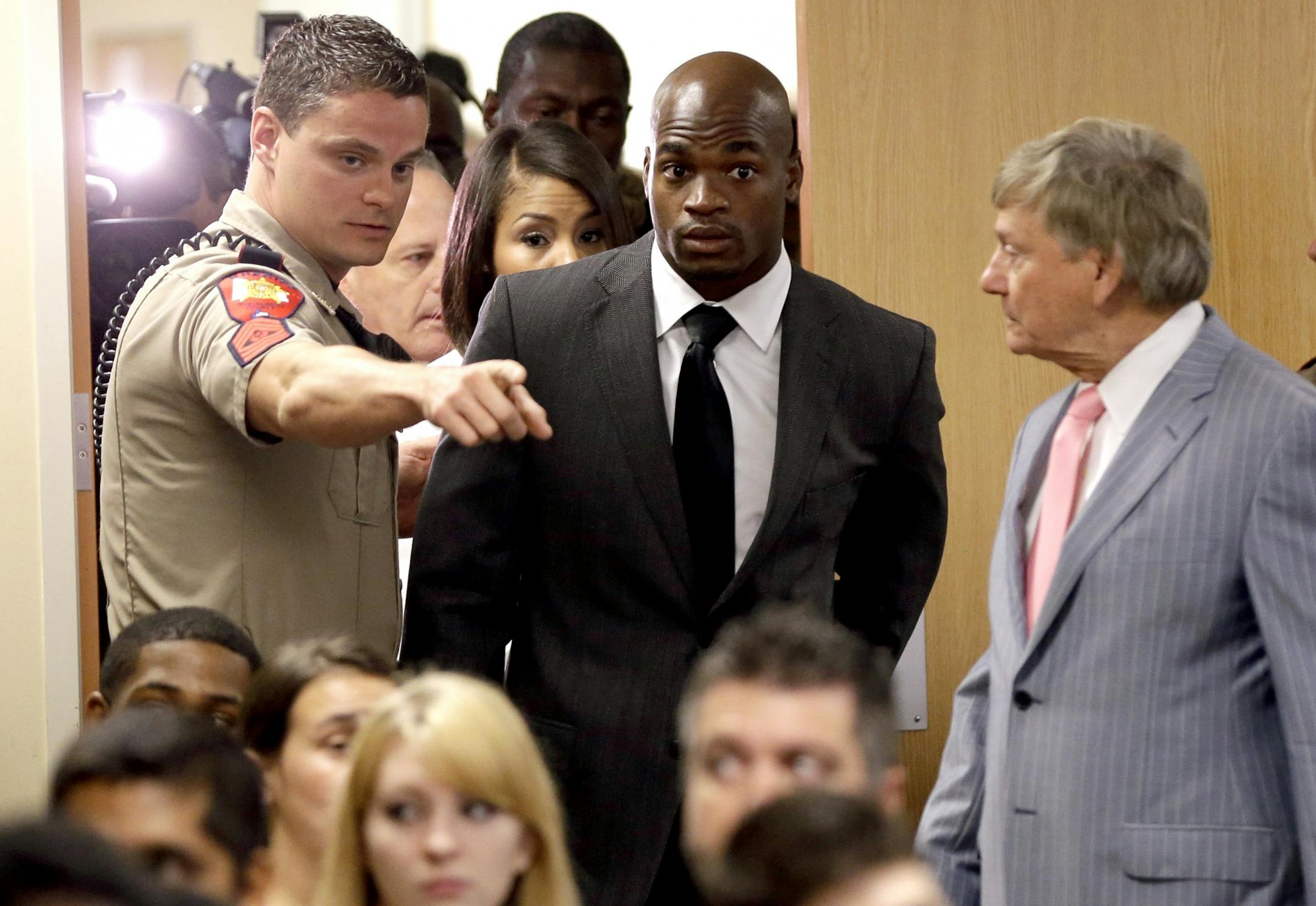 Minnesota Vikings running back Adrian Peterson, center, arrives with his attorney Rusty Hardin, right, for his first court appearance Wednesday, Oct. 8, 2014, in Conroe, Texas A Texas judge has tentatively set a Dec. 1 trial date for Peterson on a charge of felony child abuse for using a wooden switch to discipline his 4-year-old son.