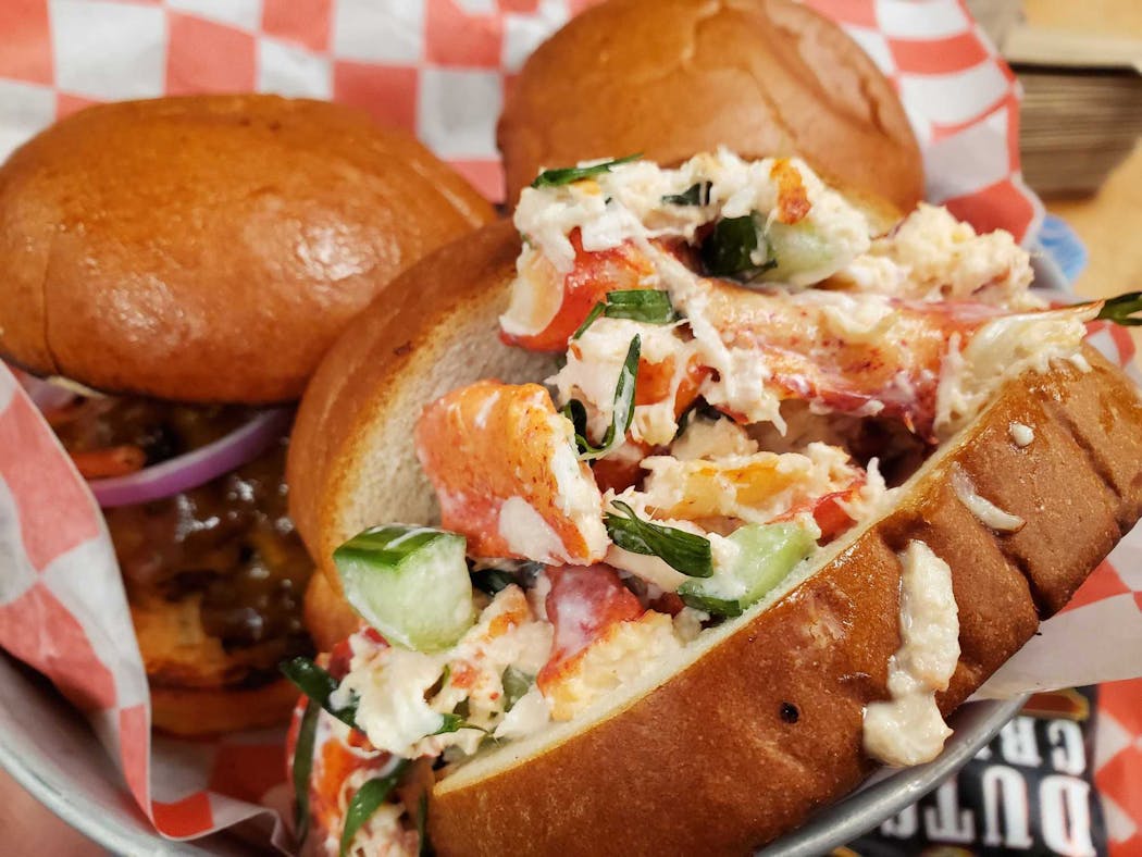 Lobster roll (foreground) and burgers (background) from Smack Shack and Burger Dive, two of the vendors at Potluck food hall in Rosedale Center