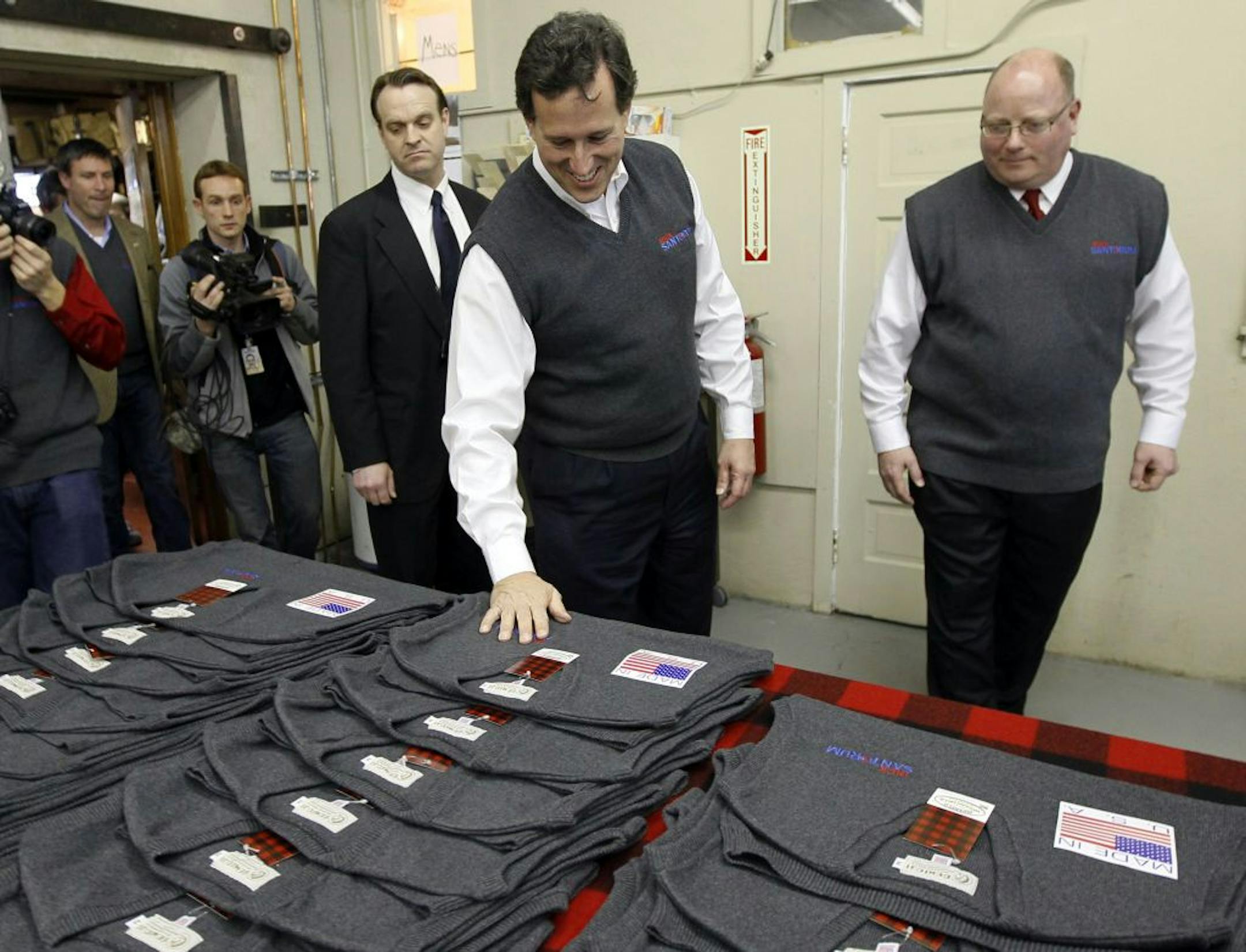 Republican presidential candidate former Pennsylvania Sen. Rick Santorum, center, looks at a display of his official, Santorum for president sweater vest, at the Bemidji Wollen Mills store, with owner Bill Batchelder, right, during a campaign stop at the vest manufacturer.