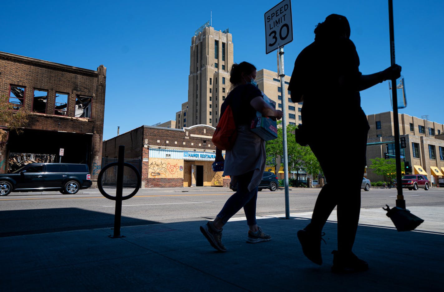 Broom-wielding volunteers walked up and down E. Lake Street, helping clean up, on Wednesday. Behind them are the burned-out Foot Locker store, looted Hamdi Restaurant and Midtown Global Market, which had broken windows