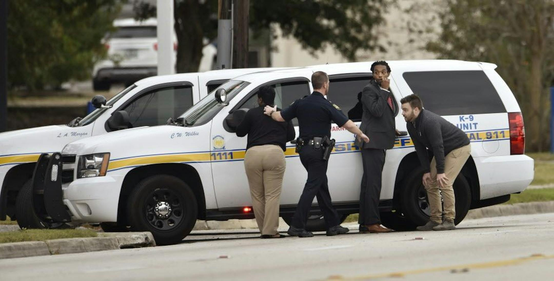 An officer stands behind a police vehicle with hostages, who fled after a gunman held them during an attempted robbery, at Community First Credit Union Thursday, Dec. 1, 2016, in Jacksonville, Fla.