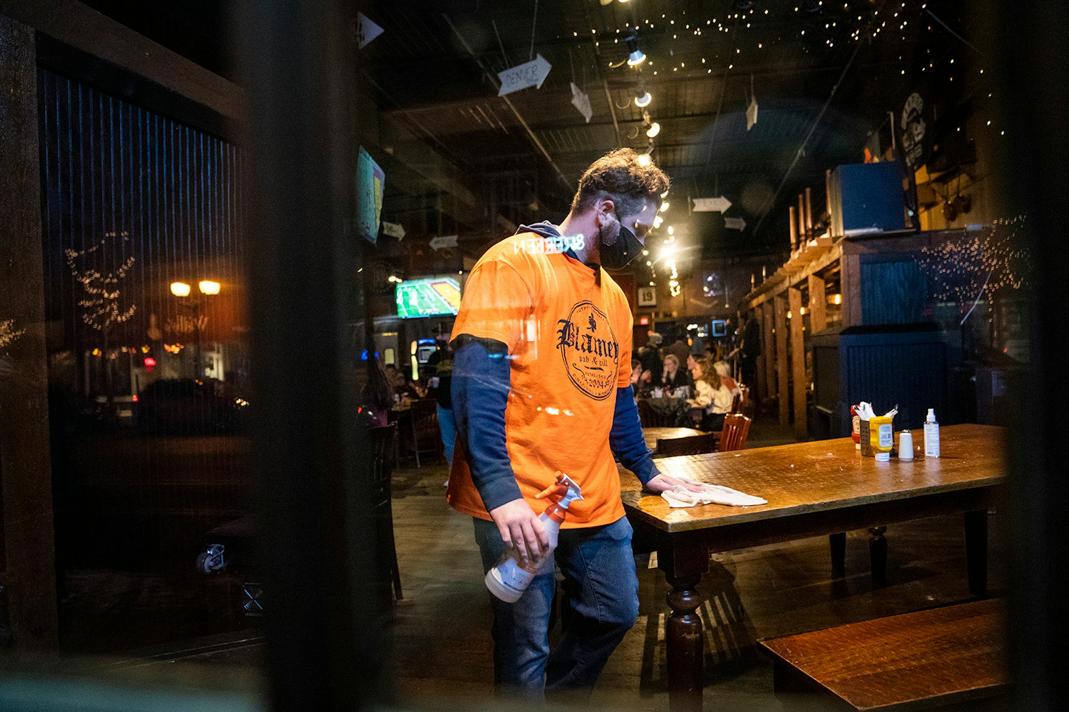 A masked employee cleaned a table at Blarney Pub & Grill in Dinkytown on Nov. 13. Hennepin County commissioners approved $8 million Tuesday to help struggling restaurant and bar owners.