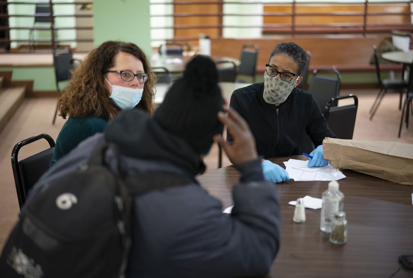 Hope Avenue program director Monica Nilsson, left, sat with Andre Jarrett while he was interviewed by Dr. Julia Joseph-Di Caprio, chief medical officer of UCare, who was volunteering in the shelter to screen clients for the COVID-19 virus Wednesday night.