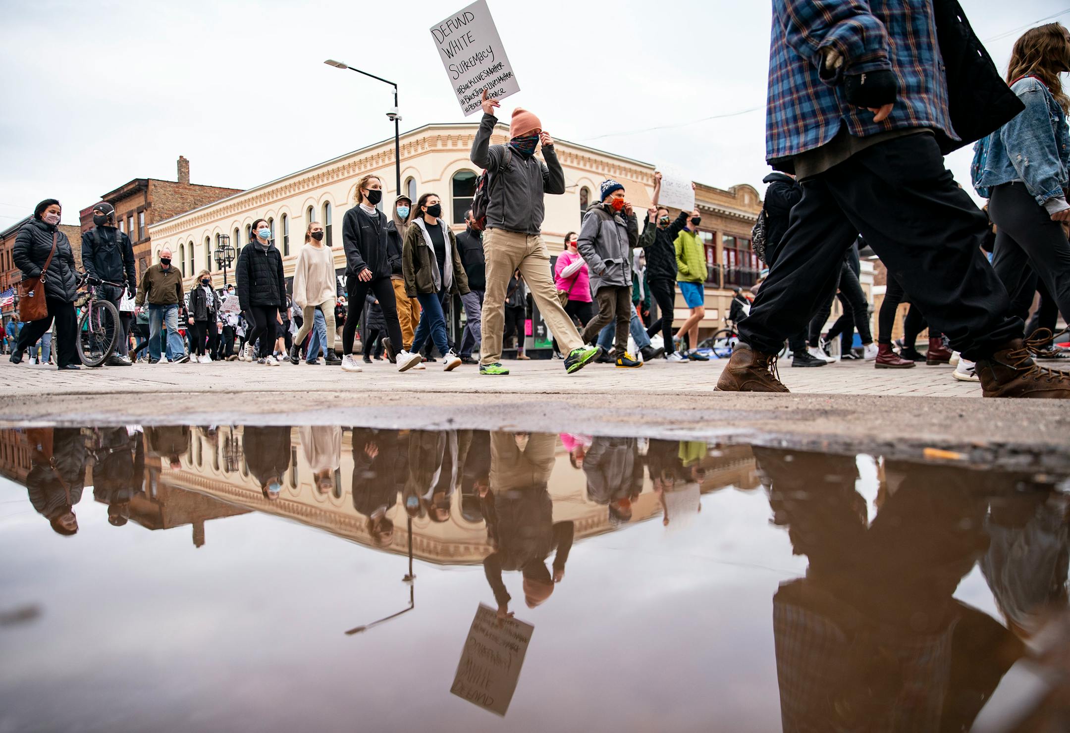 Protestors were reflected in a puddle as they marched down First St. towards Duluth City Hall on Wednesday.