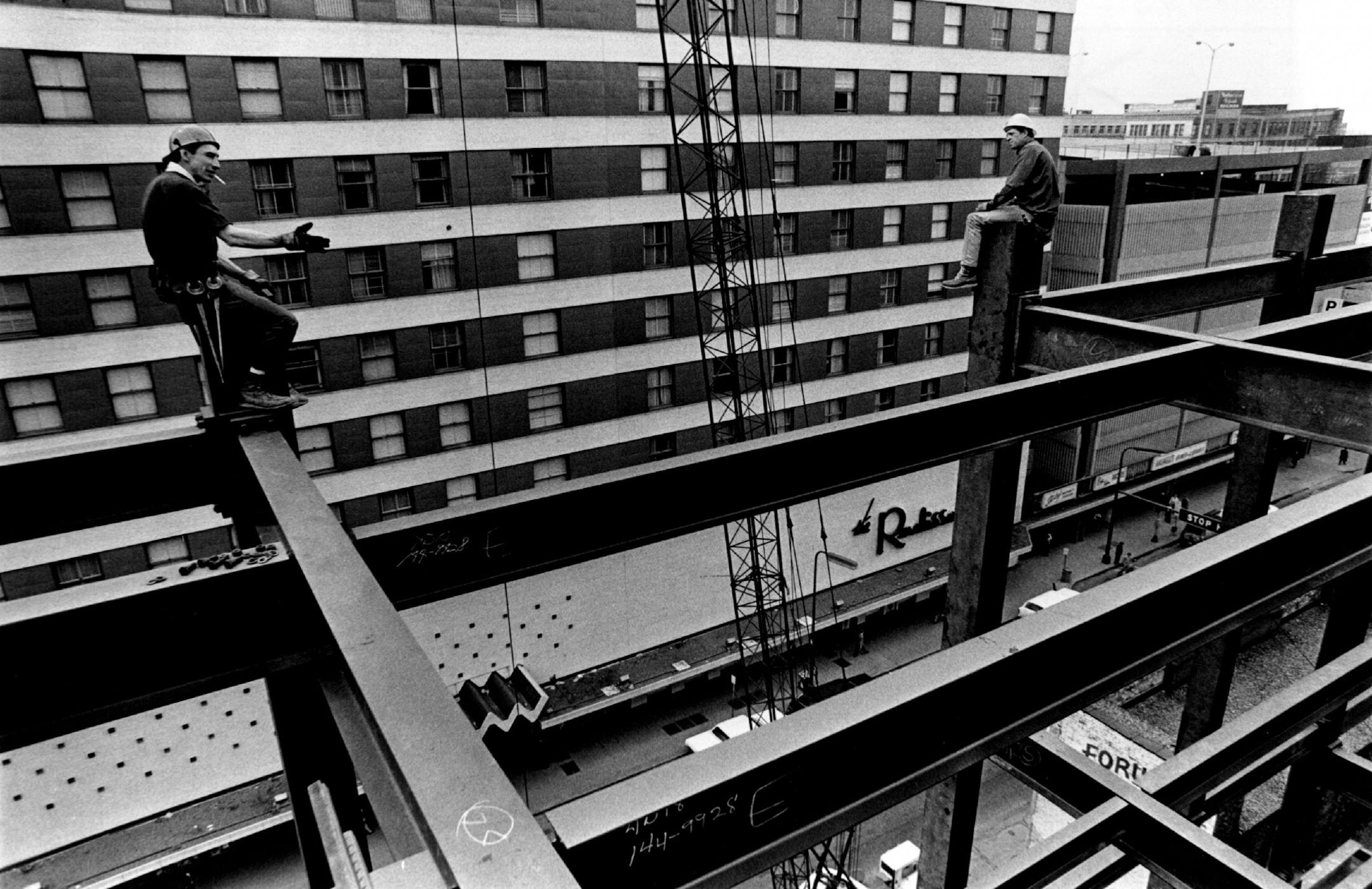 1969: High above a busy downtown Minneapolis street, two high iron workers wait for a crane to bring up a steel beam.